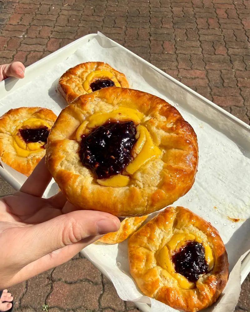 A tray of Custard & Jam Danishes, one held up to the camera